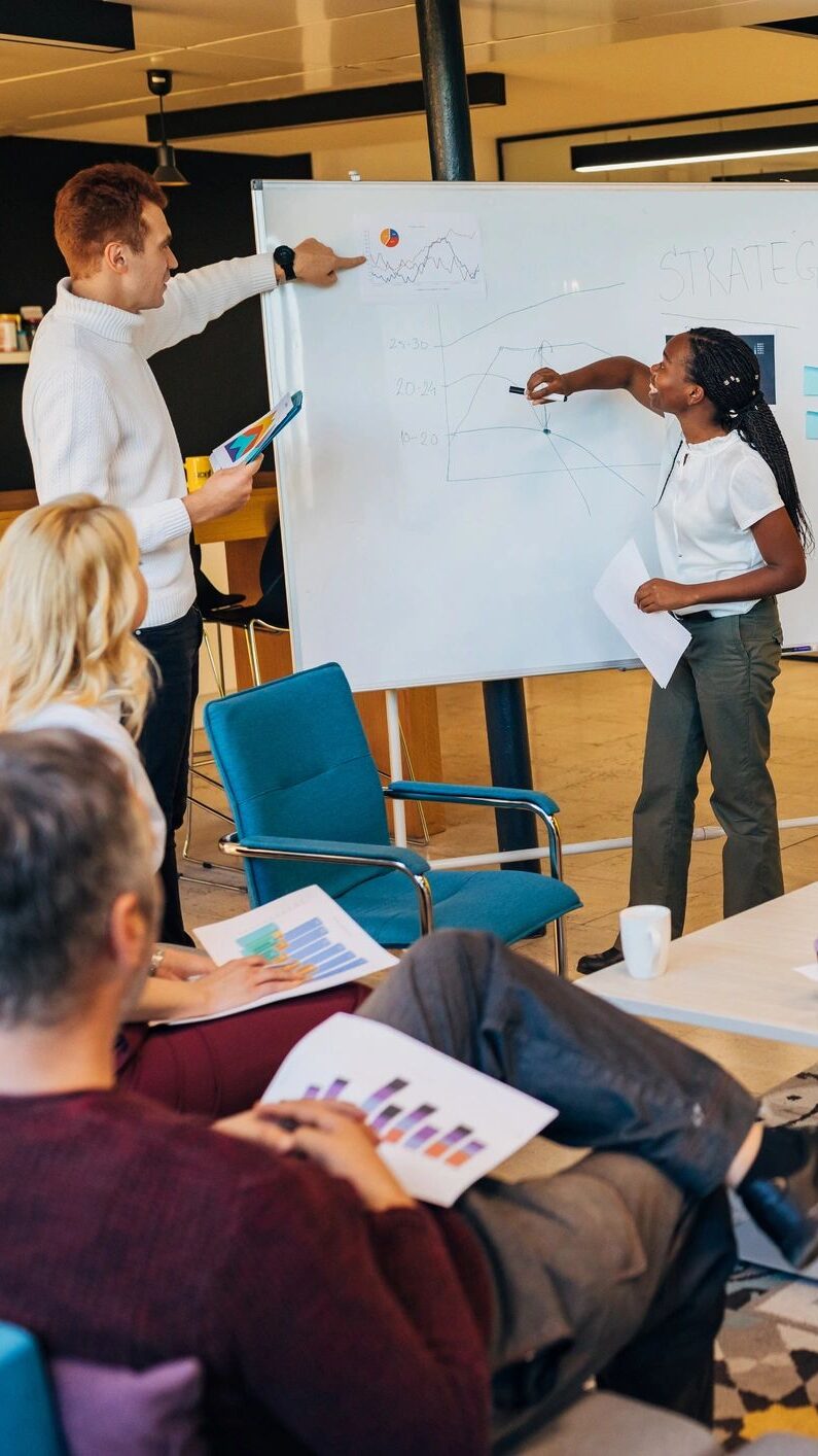 Woman Black ethnicity from finance sector writing a graph on a whiteboard so all in her team can have a better transparency about work problem